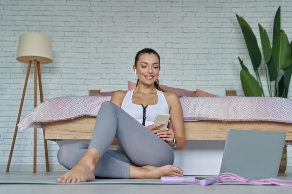 Attractive young woman in sports clothing watching online lesson before training at home