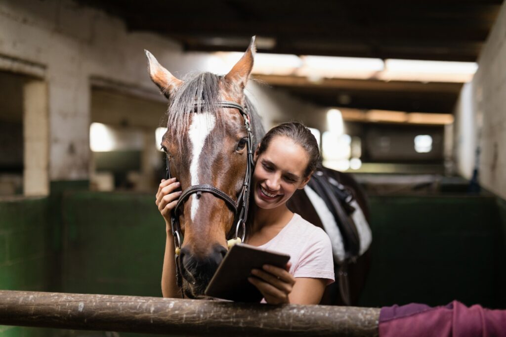 Smiling female jockey using digital tablet while standing by horse